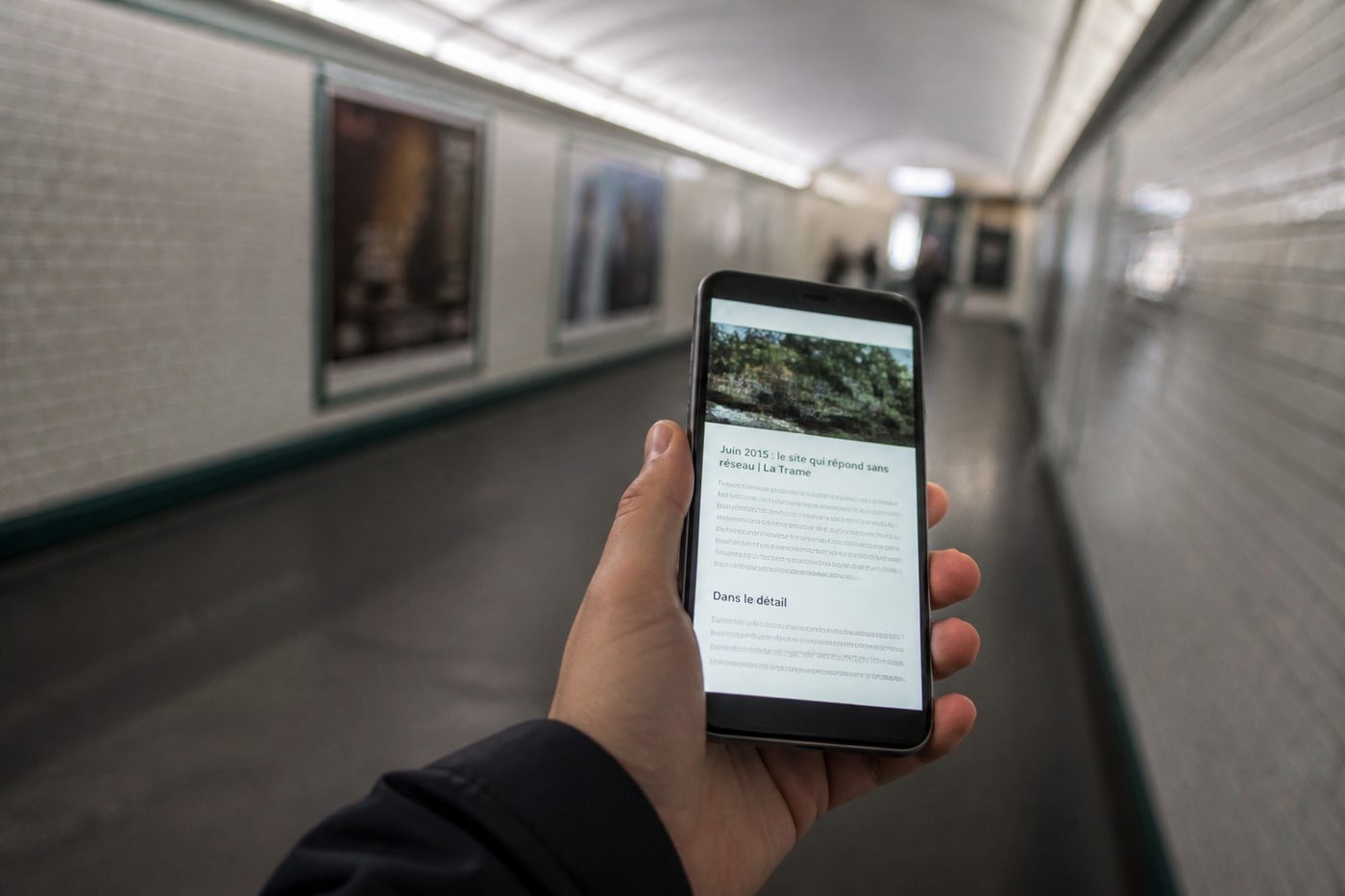 Téléphone tenu à la main dans un couloir de métro souterrain, affichant une page de contenu alors qu'aucun réseau n'est disponible.